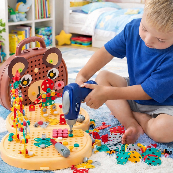 Blonder Junge im blauen T-Shirt sitzt auf einem Teppich und schraubt mit dem blauen Spielzeugbohrer an bunten Bauteilen auf der Lochplatte des Bärenkoffers. 1