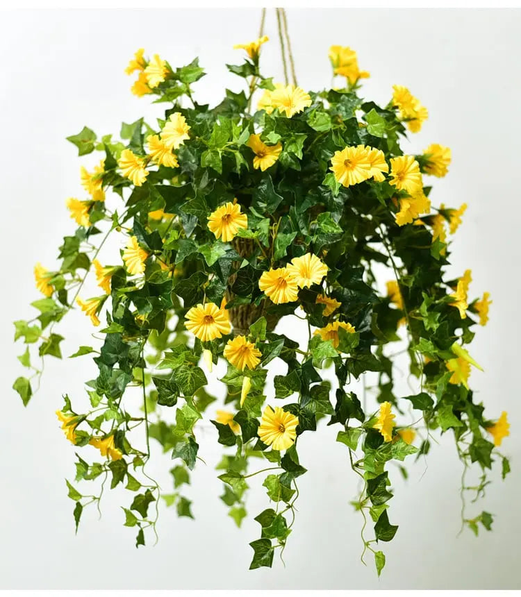 Gelbe Kunstblüten mit dichtem dunkelgrünem Blattwerk, an Seilen hängend vor hellem Hintergrund, lange Ranken fallen nach unten. 2