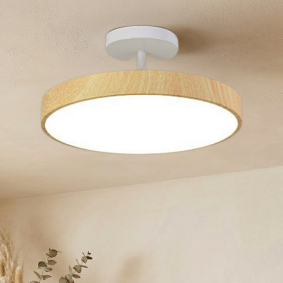 Leuchte mit heller Holzoptik und weißer Deckenhalterung, eingeschaltet in kühlerem Weiß, an einer Decke mit Eukalyptuszweigen. 4