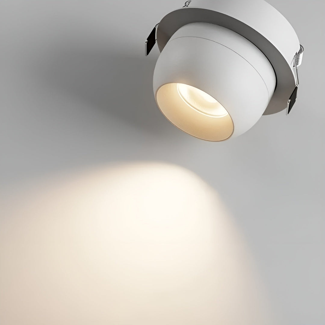 Nahaufnahme eines weißen Einbaustrahlers mit sichtbaren Federklammern, der einen warmen Lichtkegel an die Wand wirft 4