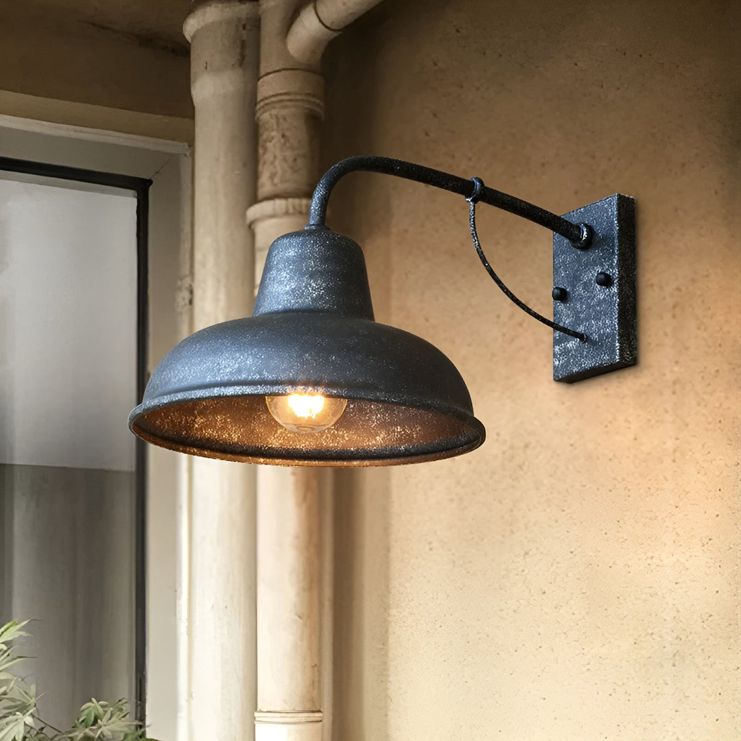 Wandlampe mit verwittertem, körnigem Finish brennt an einer sandfarbenen Wand neben einem alten Fallrohr, nahe einem Fenster. 6