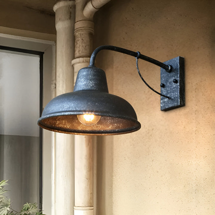 Wandlampe mit verwittertem, körnigem Finish brennt an einer sandfarbenen Wand neben einem alten Fallrohr, nahe einem Fenster. 6