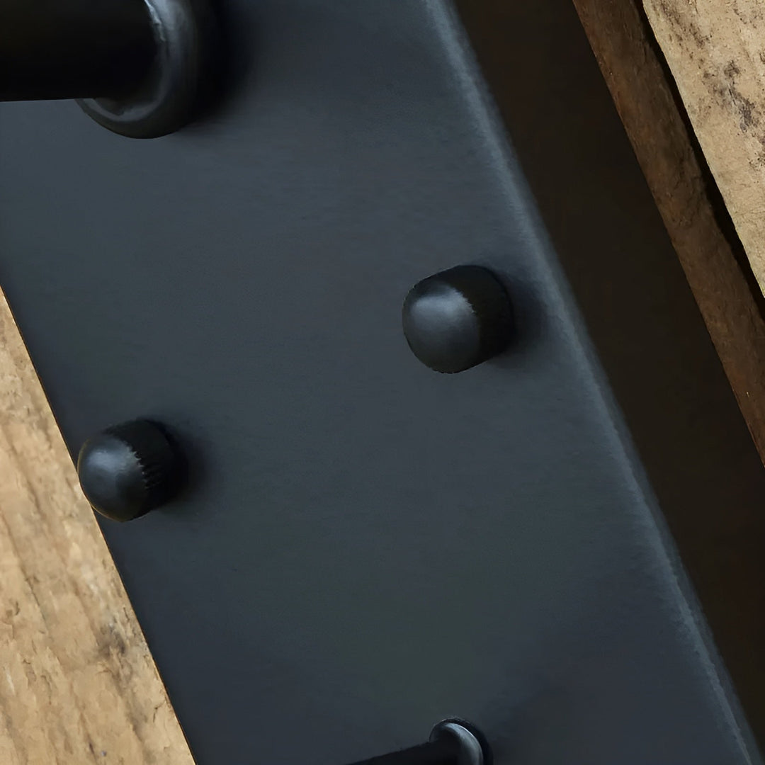 Nahaufnahme der schwarzen Wandplatte mit zwei runden Nietköpfen und dem Ansatz des Arms, im Hintergrund Holz. 7