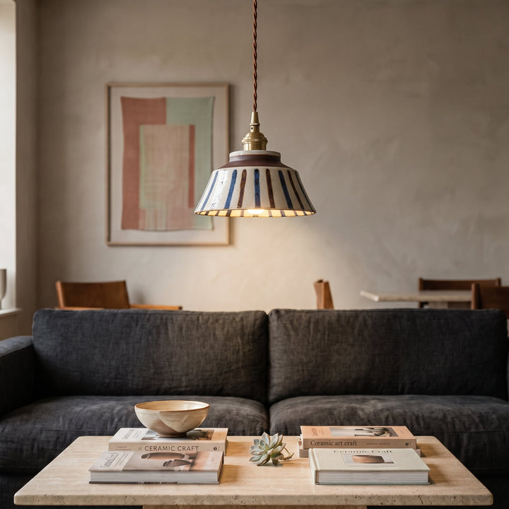 Gestreifte Pendelleuchte über einem Couchtisch aus hellem Stein mit Büchern und Keramikschale vor einem dunkelgrauen Sofa. 5