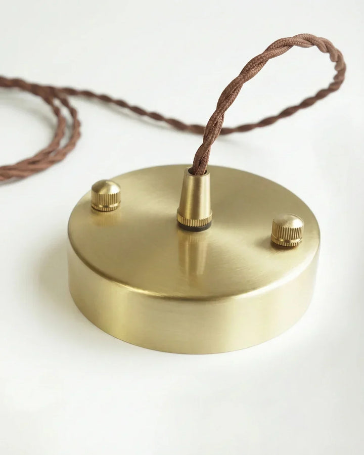 Runde Deckenrosette aus gebürstetem Messing mit zwei Schrauben und durchgeführtem verdrehtem braunem Stoffkabel auf weißem Untergrund. 8