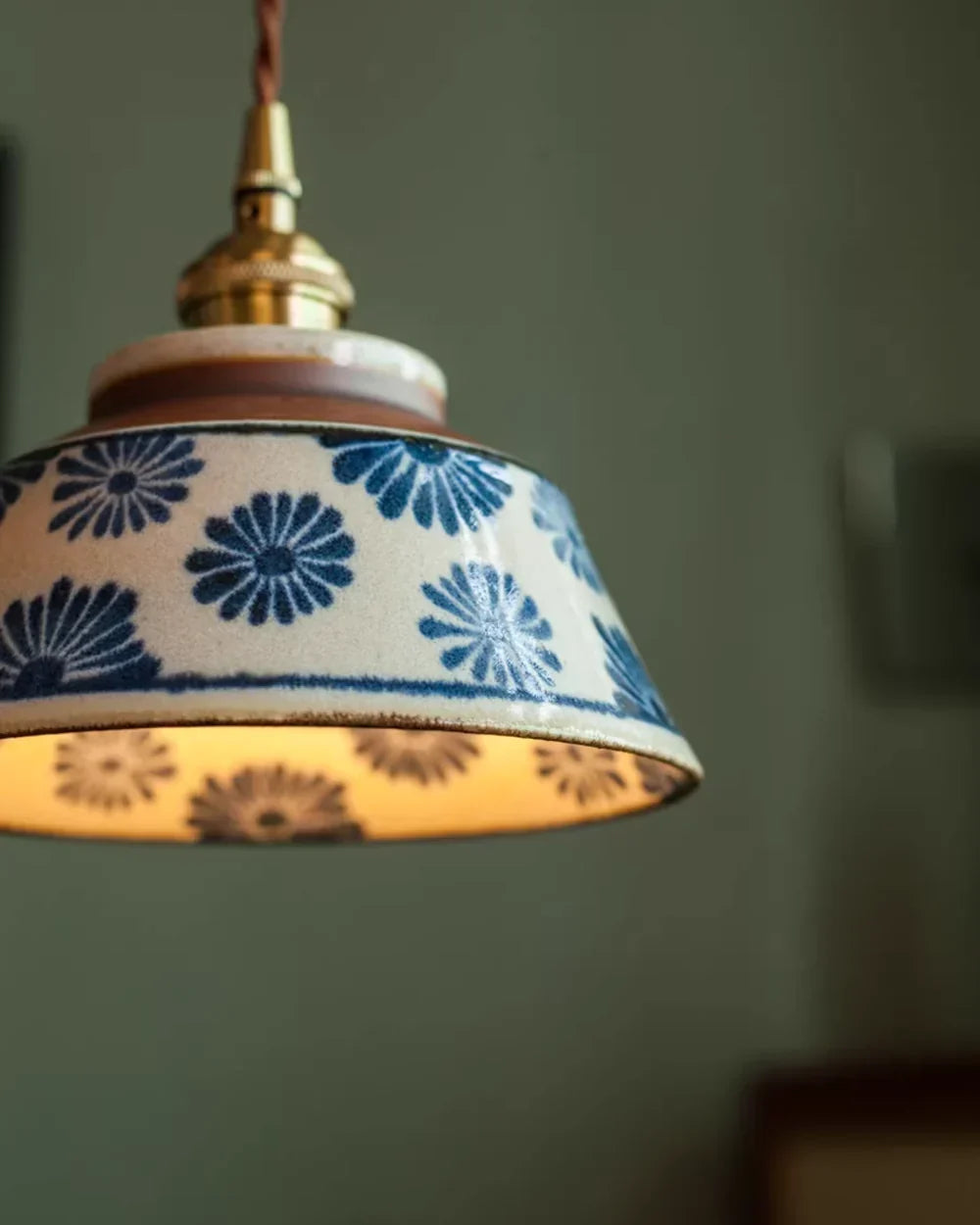 Nahaufnahme des Schirms mit blauen Blumen, glänzender Glasur und der Messingfassung am verdrehten braunen Stoffkabel. 6