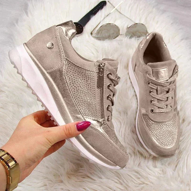 Die Schuhe in Taupe auf weißem Fell, ein Schuh von einer Hand gehalten, daneben Sonnenbrille und Uhr, Seitenansicht mit Reißverschluss. 7