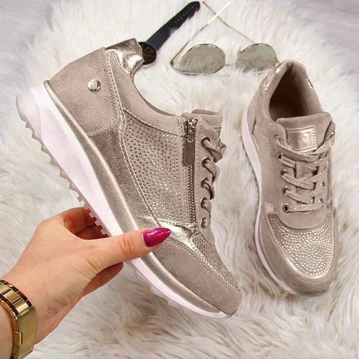Die Schuhe in Taupe auf weißem Fell, ein Schuh von einer Hand gehalten, daneben Sonnenbrille und Uhr, Seitenansicht mit Reißverschluss. 7