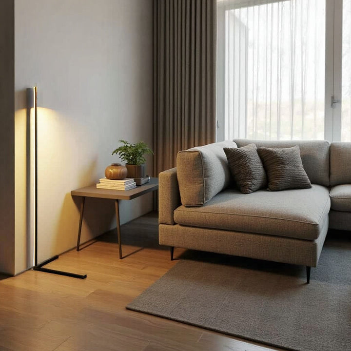Stehlampe mit warmem Licht an heller Wand, daneben ein kleiner Tisch mit Pflanze und ein graues Ecksofa 6