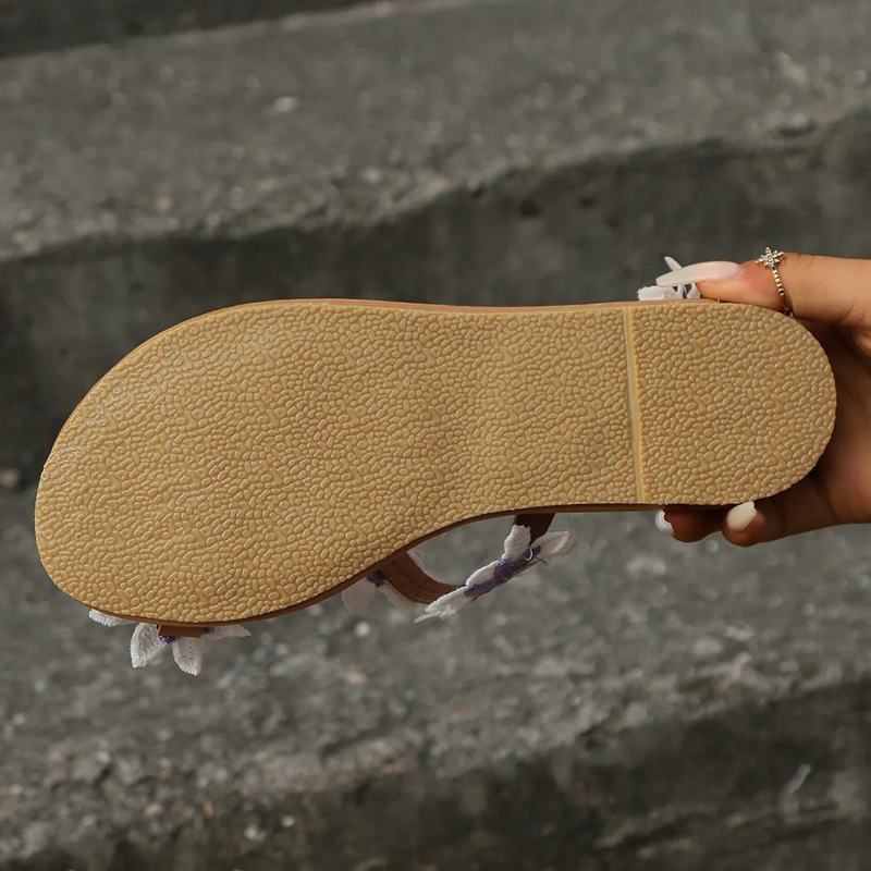 Beige Sandalensohle aus Gummi, rutschfest, in Hand gehalten, auf grauem Hintergrund.