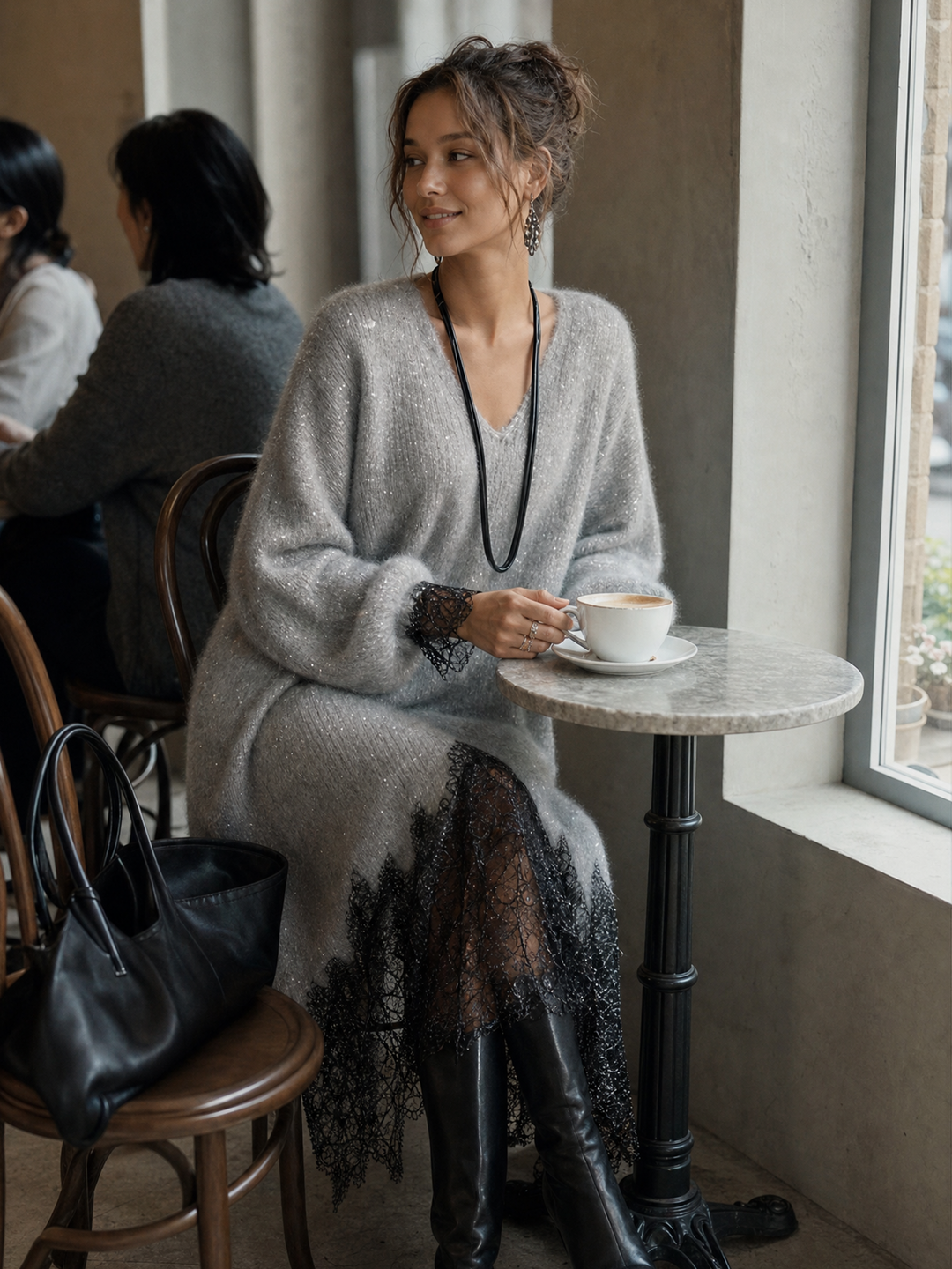 Model sitzt im grauen Strickkleid mit Spitzensaum an einem Caféfenster und hält eine Kaffeetasse 4