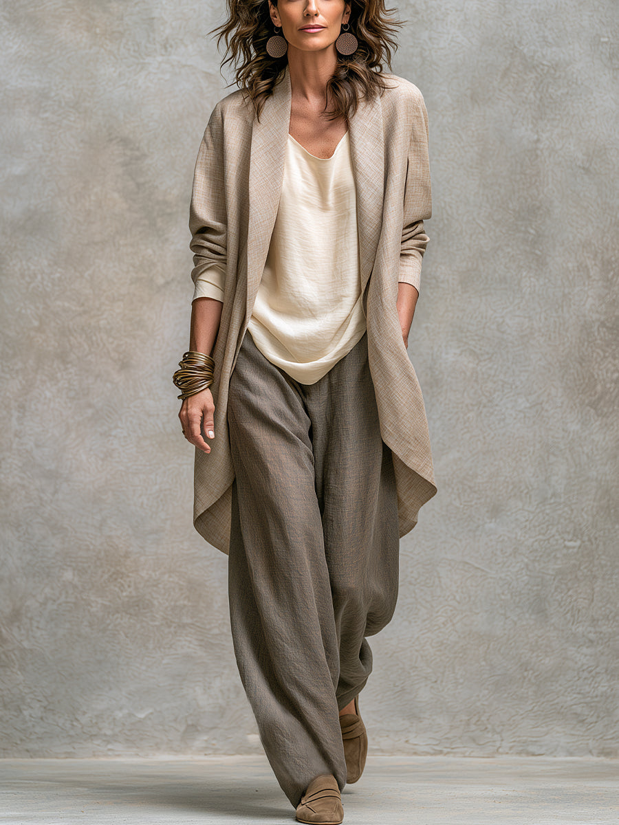 Model im kompletten Set aus beigem offenem Jackett, cremefarbenem Oberteil und grauer Weitbeinhose, ganzer Look vor Betonwand. 1