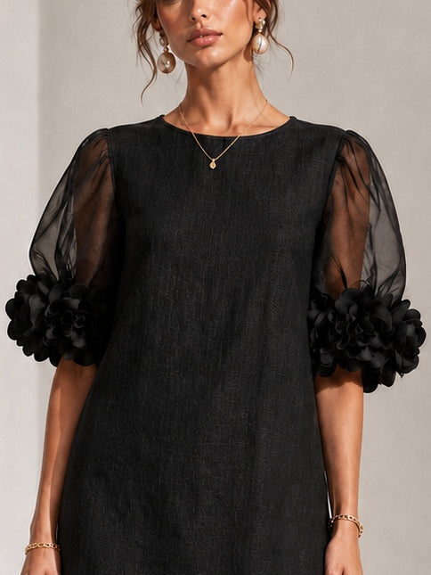 Nahaufnahme von Oberteil und Ärmeln: strukturierter schwarzer Stoff, runder Ausschnitt, transparente Puffärmel mit plastischen Blumenapplikationen. 5