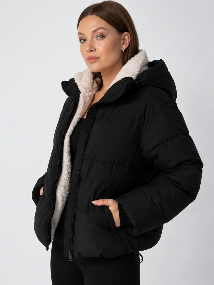 Schwarze Steppjacke von schräg vorn mit Kapuze, cremefarbenem Teddyfutter und Reiverschlusstasche 12