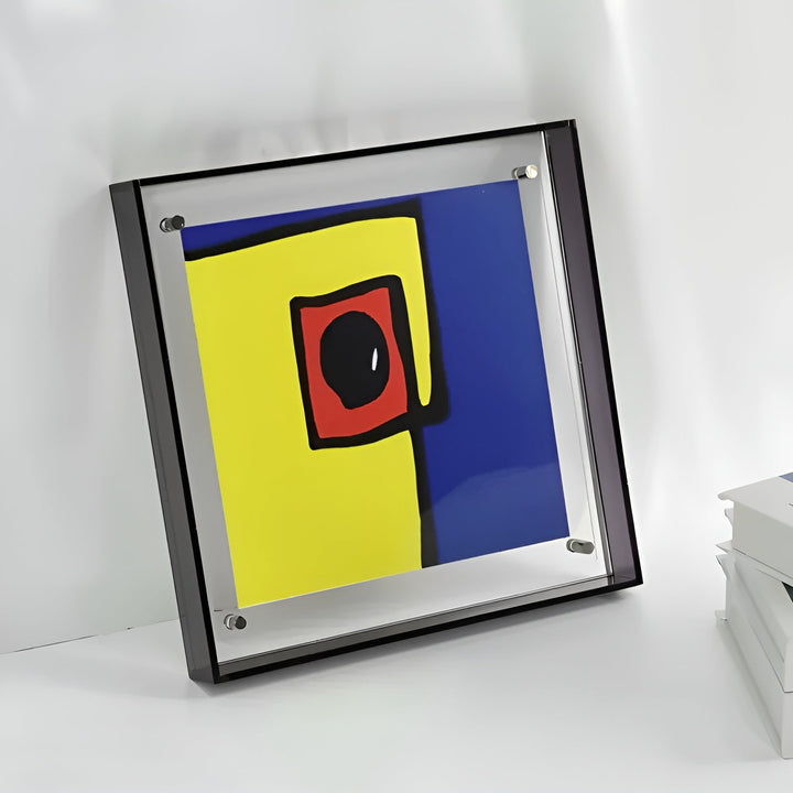 Quadratischer Rahmen mit schwarzem Acrylrand und Schraubbefestigung, darin ein abstraktes Bild in Gelb, Blau und Rot, an Wand gelehnt. 6