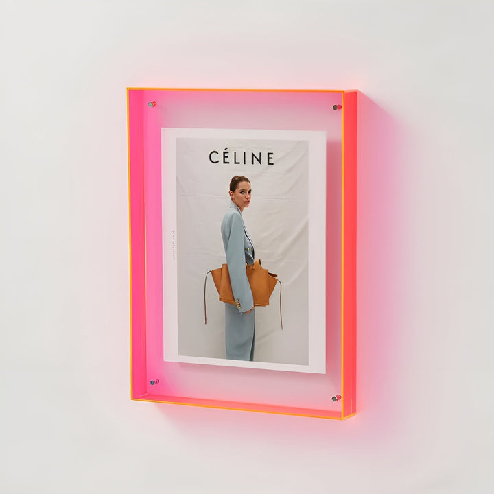 Wandmontierter Rahmen mit neonpinkem Acrylrand, darin ein Modemagazin-Motiv einer Frau im hellblauen Anzug mit brauner Tasche. 18
