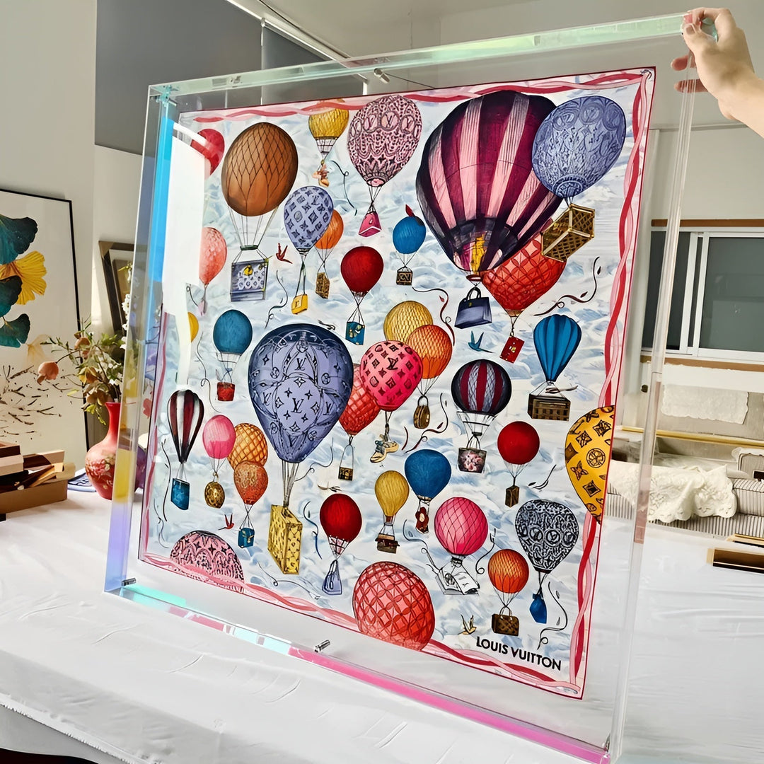 Großer transparenter Rahmen mit schimmerndem Rand, von einer Hand gehalten, darin ein farbenfrohes Tuch mit Heißluftballons. 11
