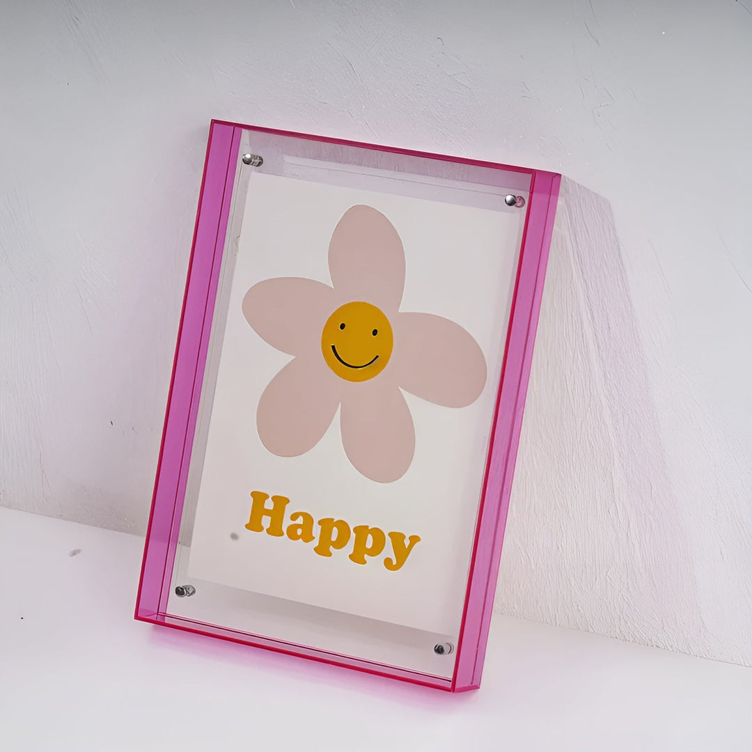 Pinker Acrylrahmen mit lächelnder Blume und gelbem Schriftzug, an eine weiße Wand gelehnt. 19