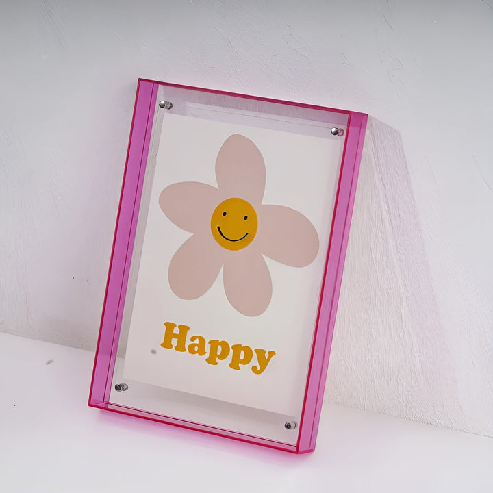 Pinker Acrylrahmen mit lächelnder Blume und gelbem Schriftzug, an eine weiße Wand gelehnt. 19