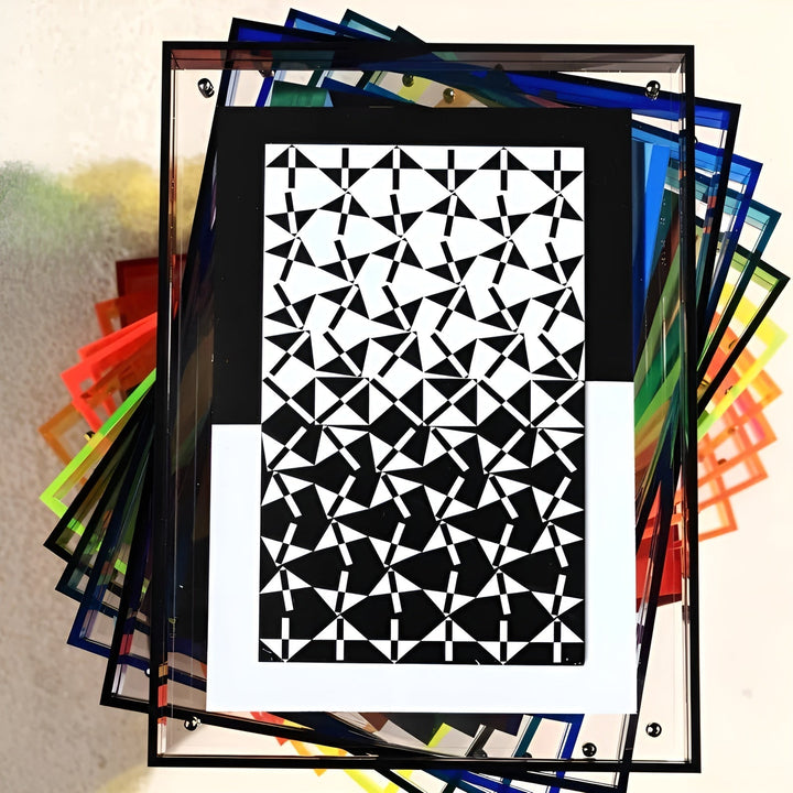 Gestapelte Acrylrahmen in verschiedenen Farben, obenauf ein schwarz gerahmter Druck mit geometrischem Schwarz-Weiß-Muster. 8