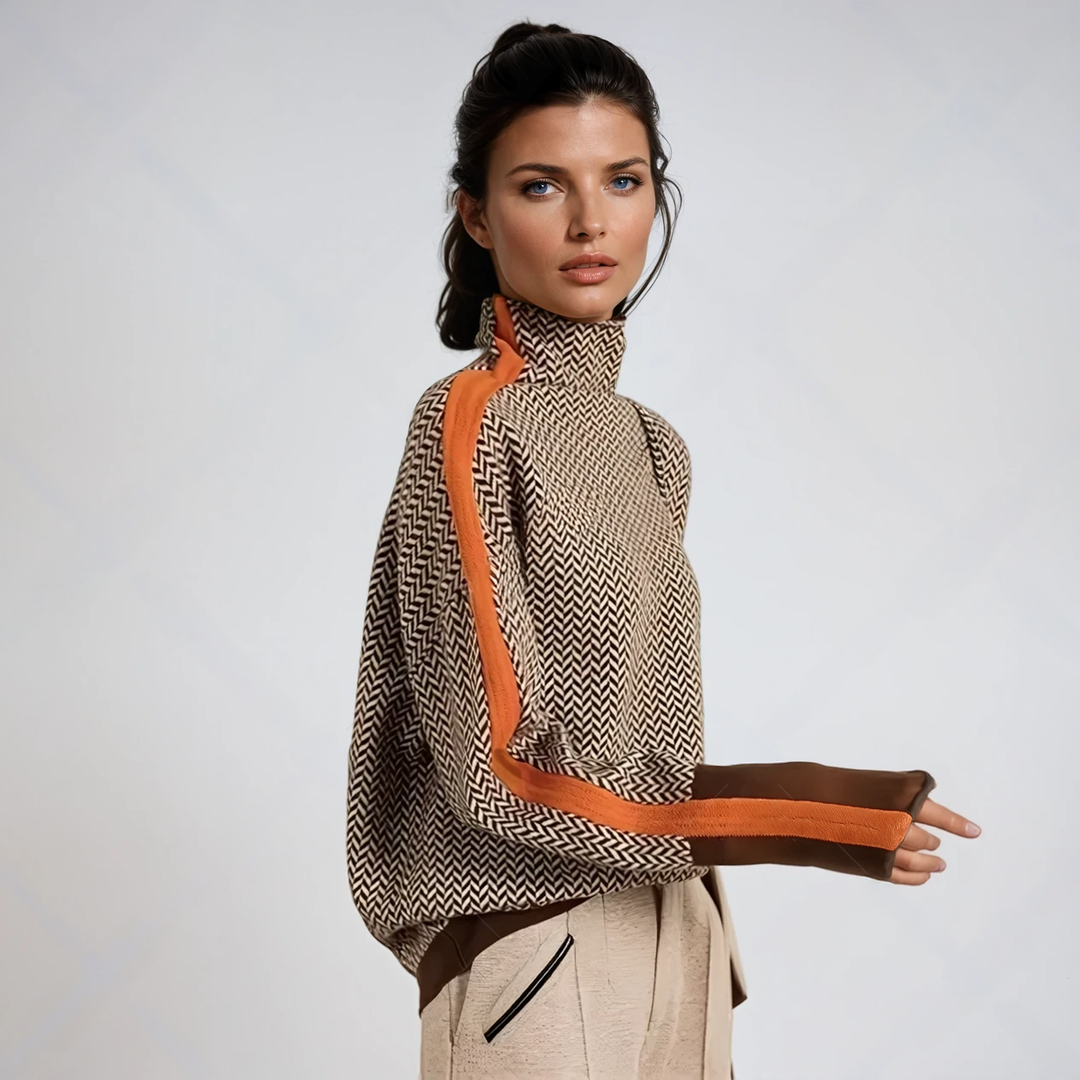 Model im Seitenprofil trägt den braun-beige Fischgrät-Pullover mit orangefarbenem Streifen am Ärmel, dazu helle Hose, vor hellem Hintergrund. 1