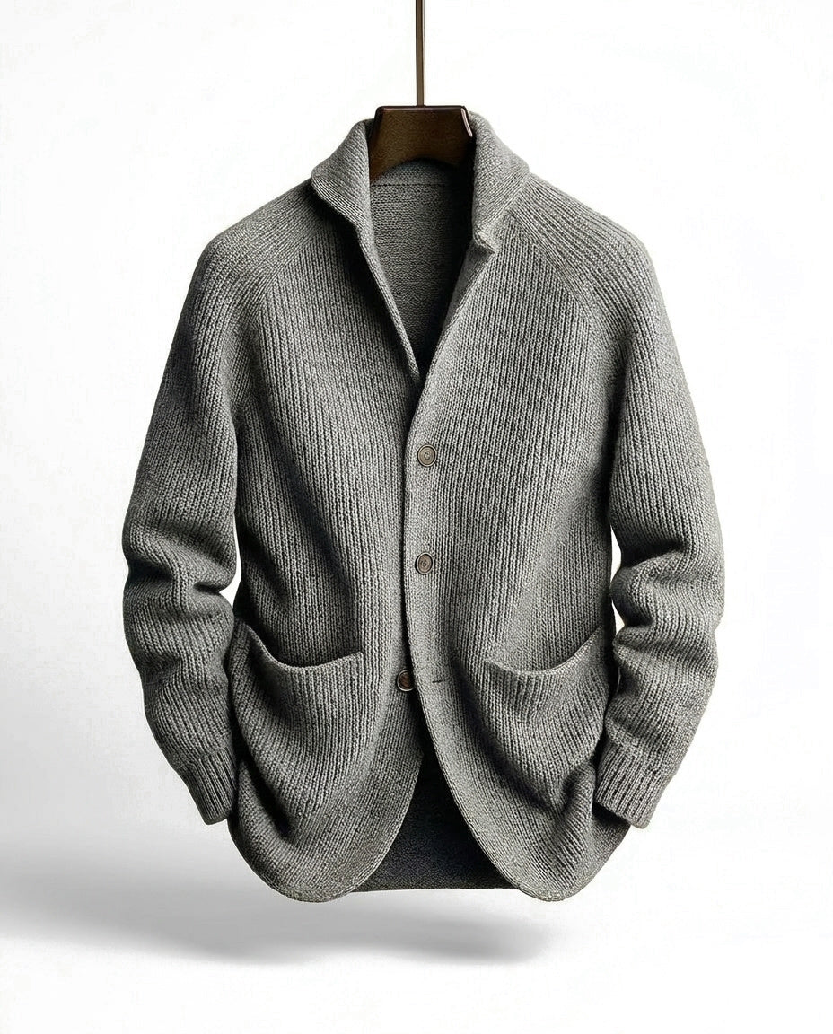 Graue Strickjacke in grober Rippstrick-Optik mit Schalkragen, Knopfleiste und Taschen, an einem Holzbügel hängend. 4
