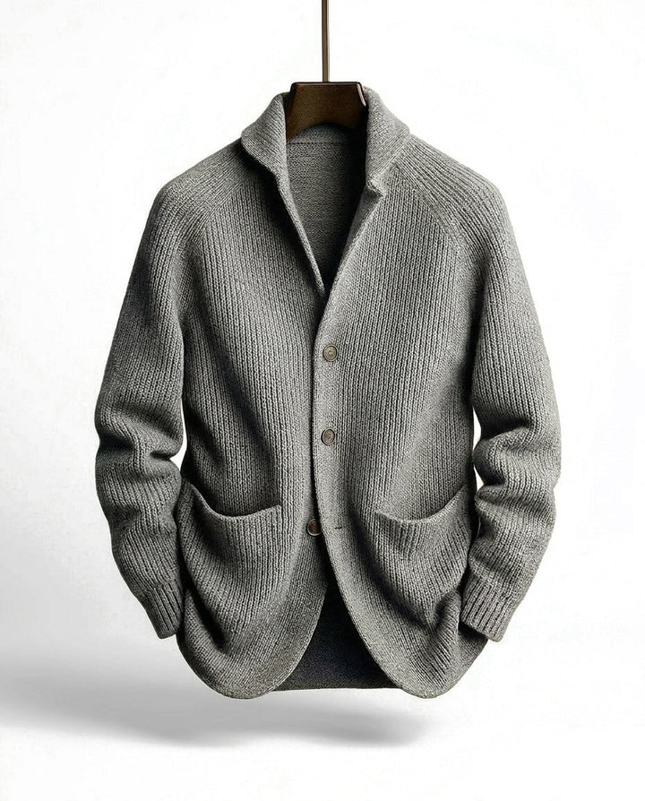 Graue Strickjacke in grober Rippstrick-Optik mit Schalkragen, Knopfleiste und Taschen, an einem Holzbügel hängend. 4
