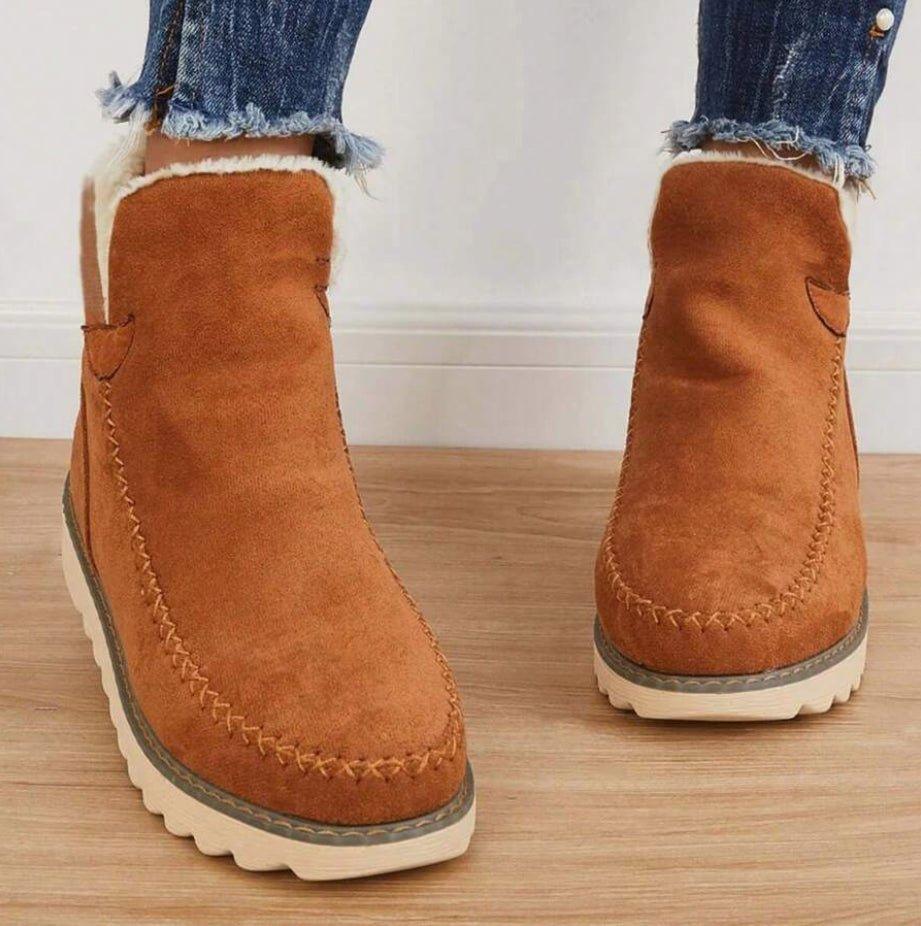 Frontansicht brauner Stiefeletten in Wildleder-Optik mit Plüschfutter und orangefarbener Ziernaht, getragen zu ausgefransten Jeans. 5