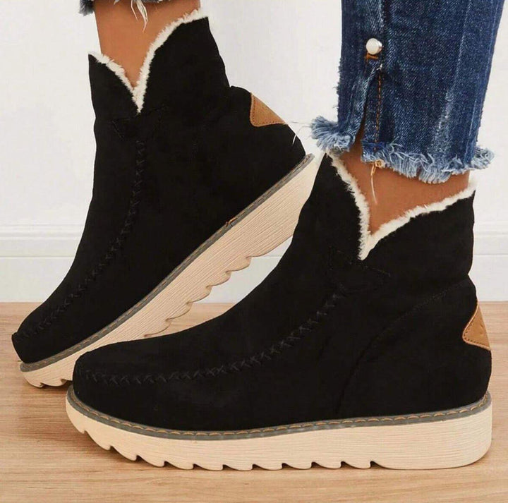 Seitenansicht schwarzer Stiefeletten in Wildleder-Optik mit weißem Fellrand, Zierstichen und profilierter heller Sohle, getragen zu Jeans mit ausgefranstem Saum 1