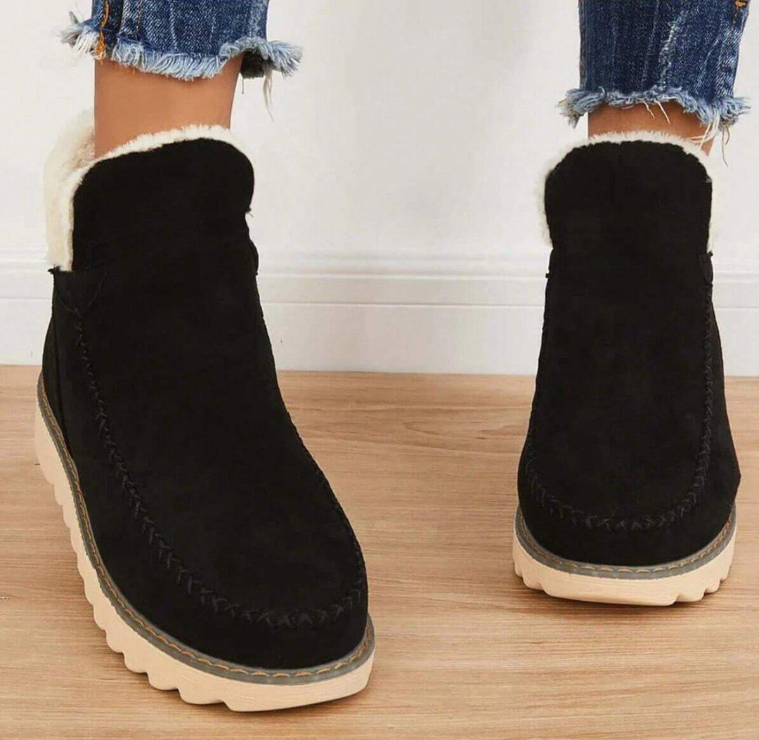 Frontansicht schwarzer Stiefeletten mit flauschigem weißem Futter und genähter Ziernaht an der Spitze, getragen mit ausgefransten Jeans. 4