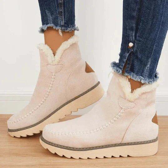 Beige Stiefeletten mit kuscheligem Fellkragen und kleinem braunem Fersenstück, an den Füßen einer Frau in Jeans von der Seite zu sehen. 3
