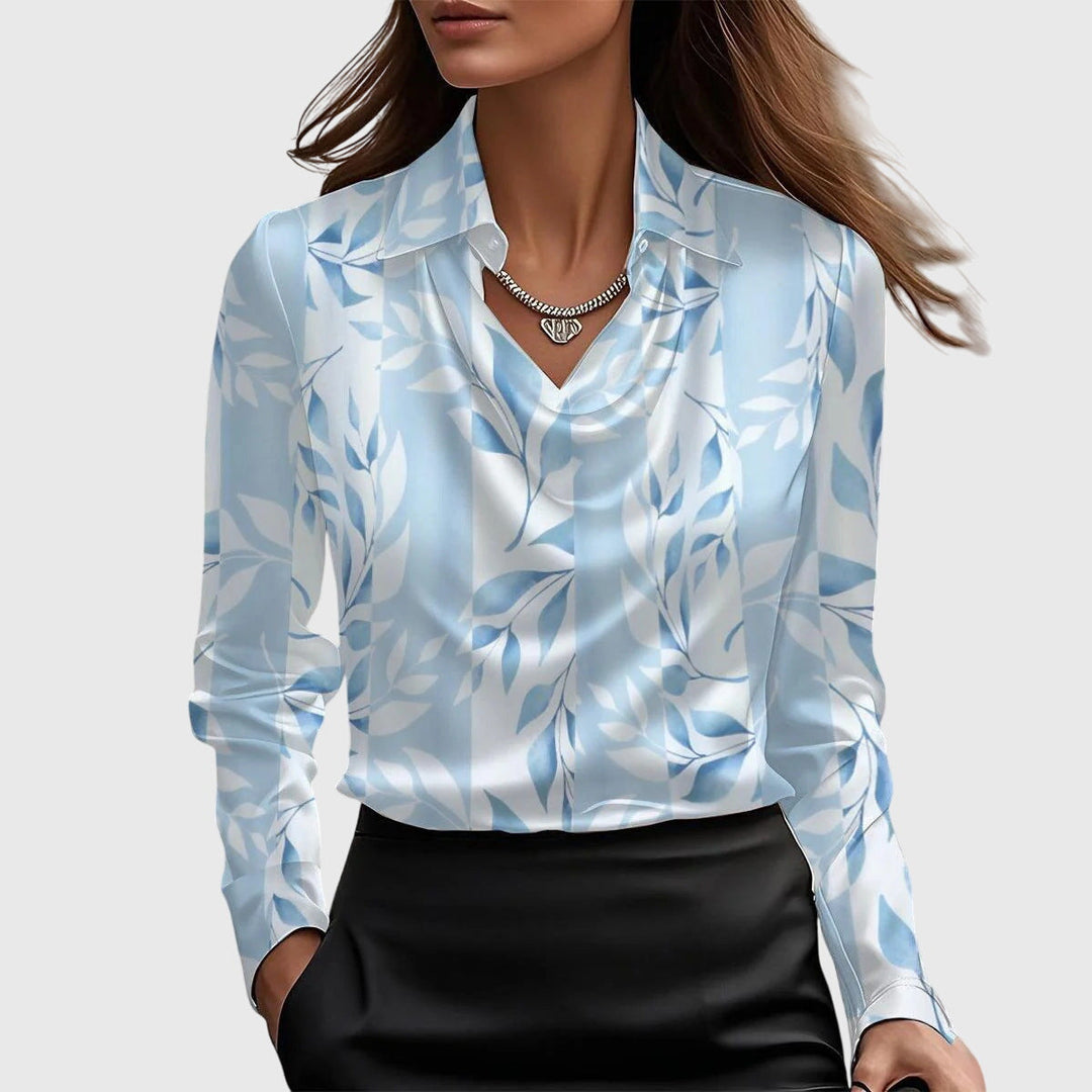 Die Bluse mit hellblauem Blattmuster auf weißem Grund, langen Ärmeln und Wasserfallausschnitt, am Model zum schwarzen Rock. 5