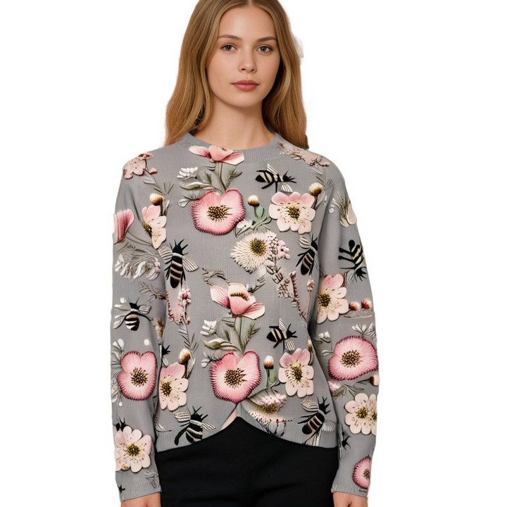 Frau in grauem Pullover mit Blumenmuster, rosa Akzenten, Bienenmotiv, modisch, elegant.