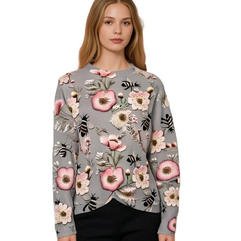 Frau in grauem Pullover mit Blumenmuster, rosa Akzenten, Bienenmotiv, modisch, elegant.