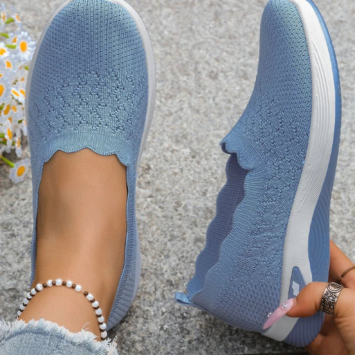 Draufsicht auf hellblaue Strick-Slip-ons mit Wellenrand, ein Fuß steckt im Schuh 16
