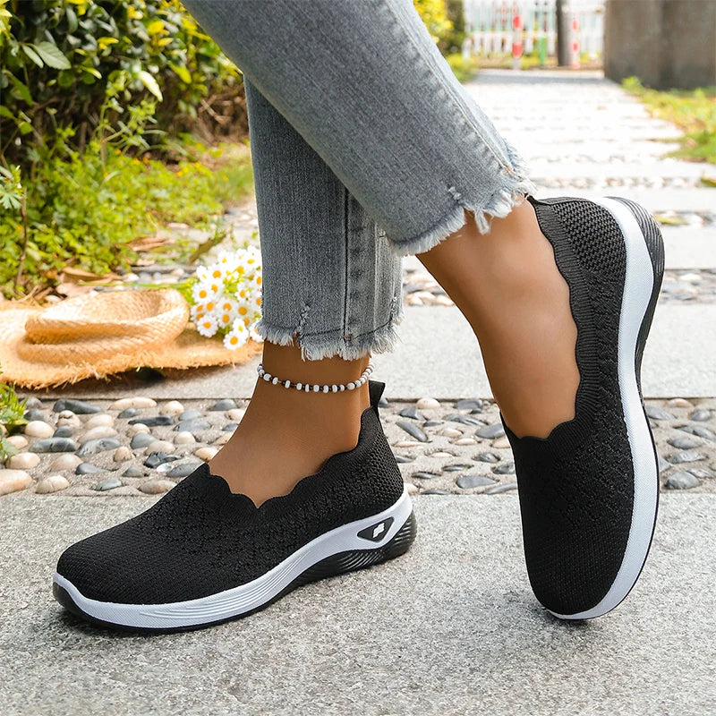 Schwarze Strick-Slip-ons mit Wellenrand, seitlich fotografiert beim Gehen auf gepflastertem Weg 15