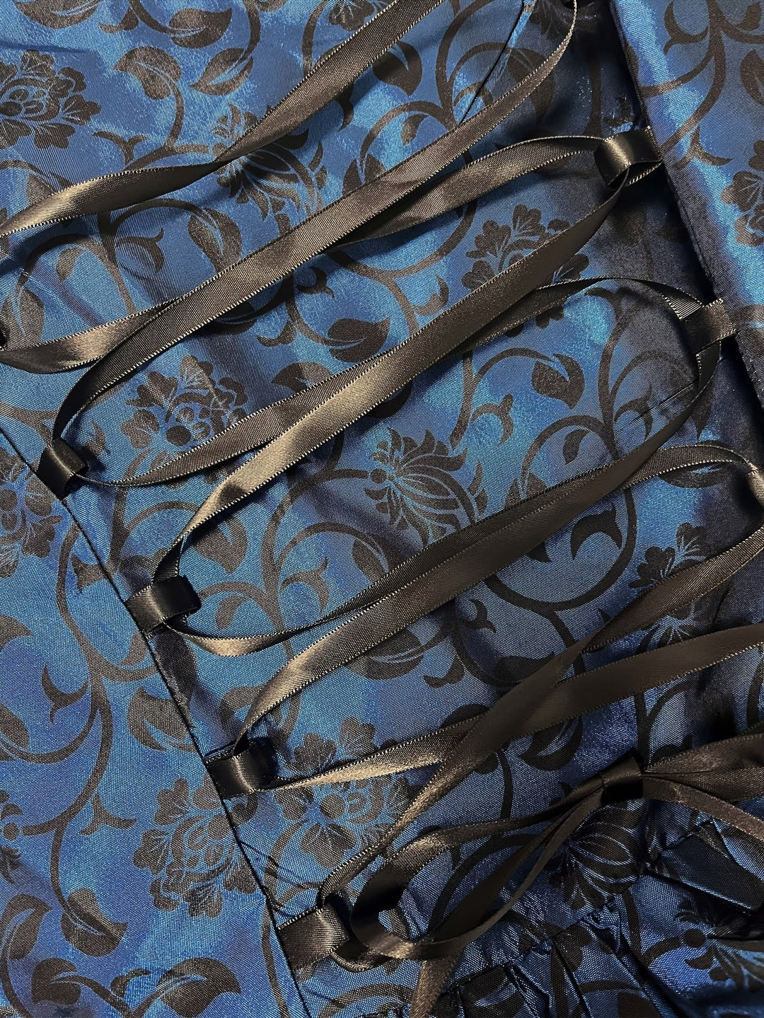 Nahaufnahme der schwarzen Satinband-Schnürung auf dem blauen Stoff mit schwarzem Blumenranken-Muster. 5