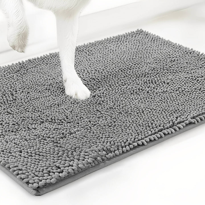 Weiße Hundepfote drückt sich in die graue Chenille-Matte, Schrägansicht der Mattenecke auf weißem Hintergrund. 12