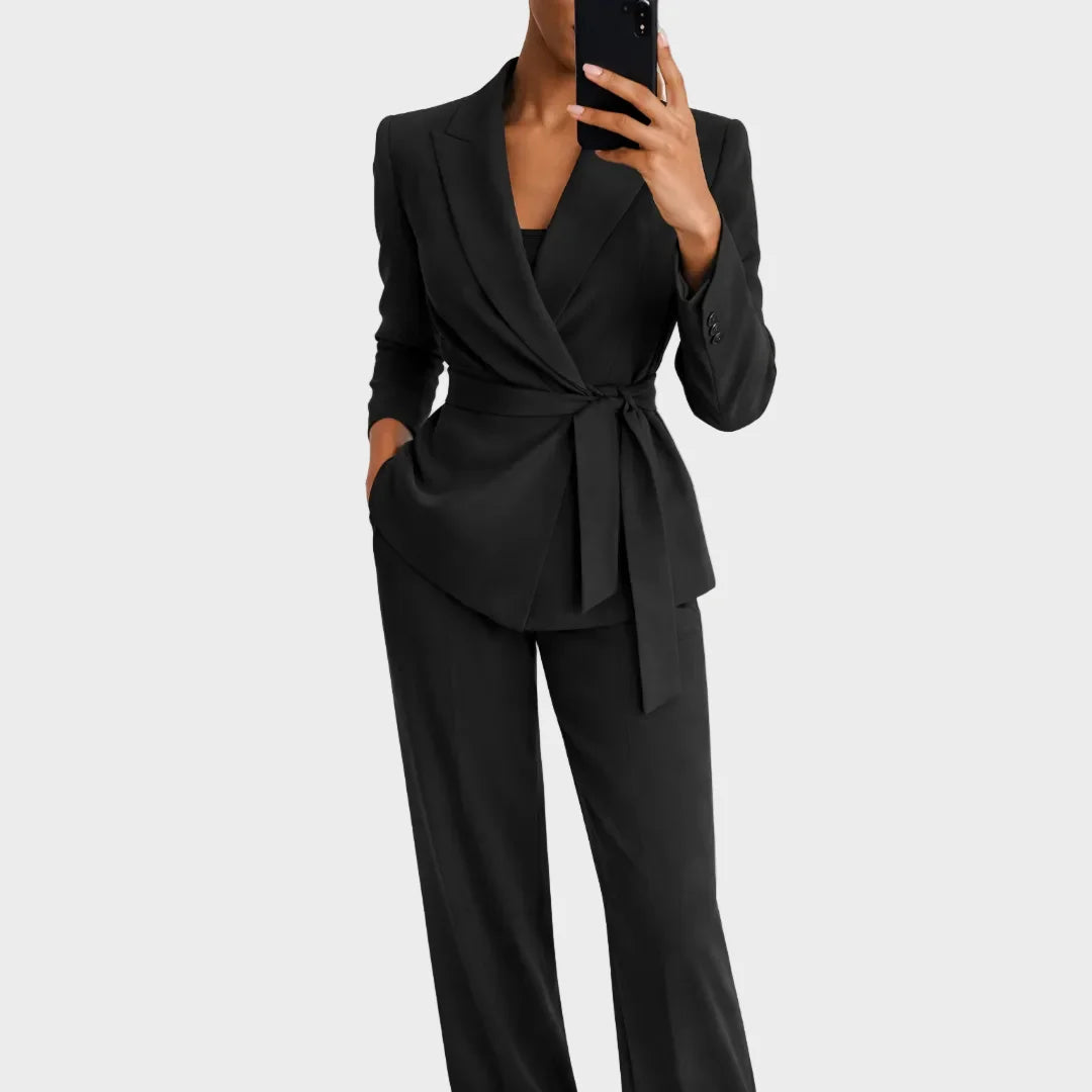 Das Set in Schwarz: Blazer mit Wickelvorderseite und Bindegürtel plus weite Hose, Frontansicht, Model fotografiert sich im Spiegel. 3