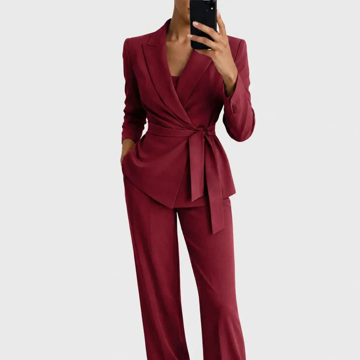 Das Set in Weinrot: Blazer mit Wickeloptik und Bindegürtel, dazu weite Hose, Frontansicht, Model hält ein Handy vor das Gesicht. 5