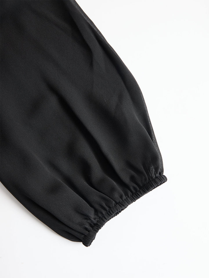 Detailansicht eines schwarzen, transparenten Ärmels aus Chiffon mit elastischem Bündchen, flach auf weißem Hintergrund ausgelegt. 4
