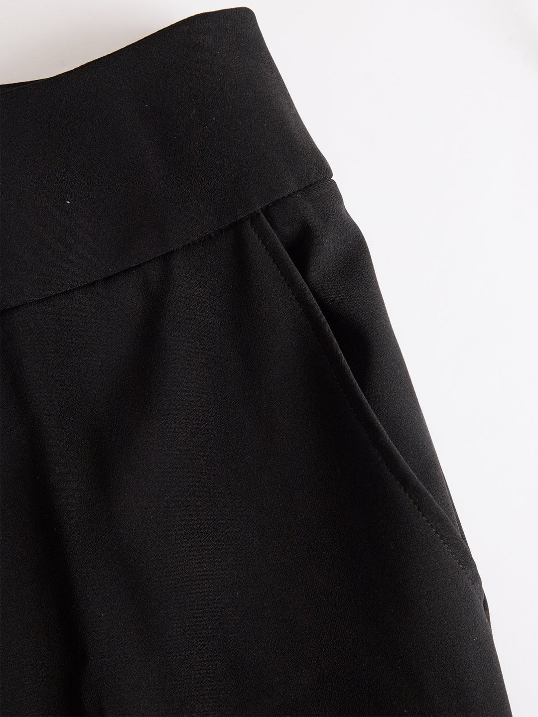 Detailansicht des breiten Bundes und der seitlichen Eingrifftasche der schwarzen Hose, flach auf weißem Hintergrund fotografiert. 5