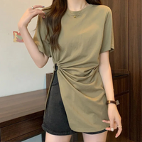 Frau in olivgrünem T-Shirt mit seitlicher Raffung, schwarze Shorts, lässiger Look.