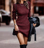 Frau in bordeauxrotem Strickkleid mit langen Ärmeln, hält schwarze Lederjacke, modisch, elegant.