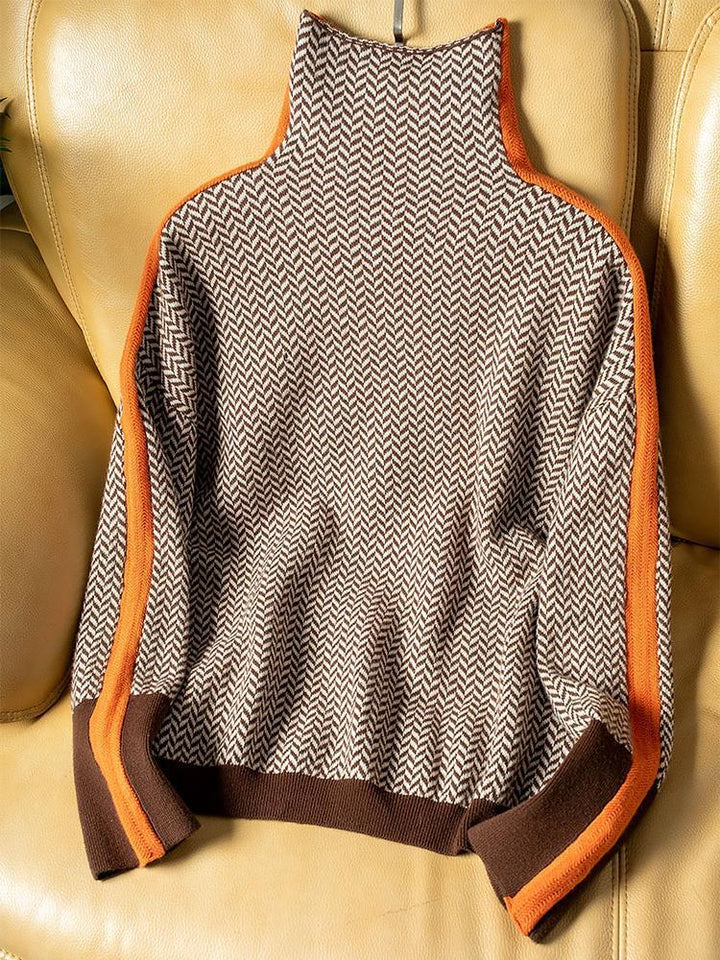 Flach auf einem hellen Ledersessel ausgebreiteter Pullover in Fischgrätmuster mit hohem Kragen, orangefarbenen Seitenstreifen und braunen Bündchen. 4