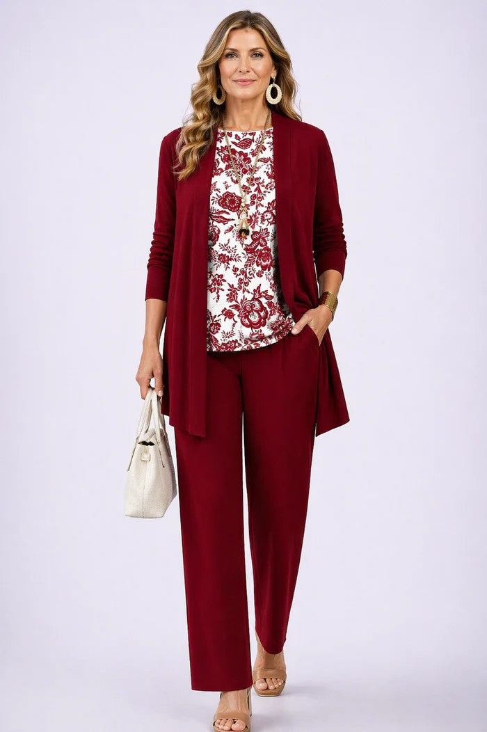 Frau im Set mit weinrotem Cardigan und Hose, dazu weißes Oberteil mit rotem Blumenmuster, Handtasche in der Hand. 13