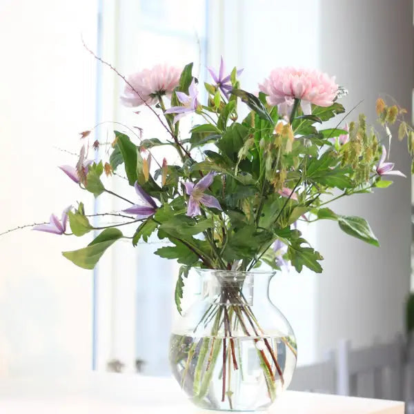 Lockerer Strauß mit rosa Dahlien und lila Clematis in einer runden Glasvase, im Wasser kreuzen sich die Stiele. 4