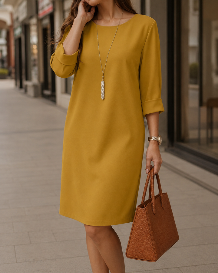 Senfgelbes Kleid mit Rundhals und Ärmelaufschlag, getragen mit langer Kette, Armbanduhr und brauner Handtasche 7