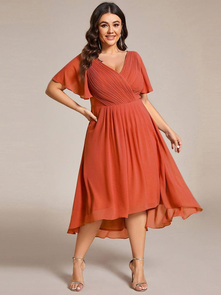 Curvy Model in terrakottafarbenem Chiffonkleid mit plissiertem V-Ausschnitt, Hand in der Hüfte, weit fallender Rock mit Vokuhila-Saum. 97