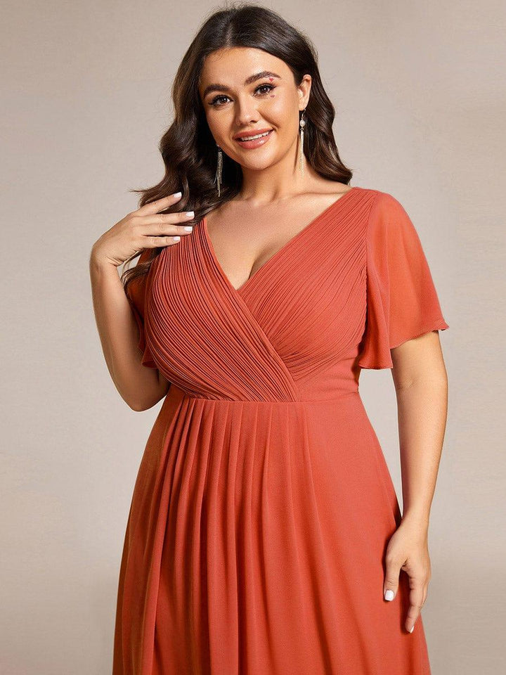 Nahaufnahme des terrakottafarbenen Kleids am Curvy Model: plissiertes Wickeloberteil, V-Ausschnitt und Flatterärmel. 99